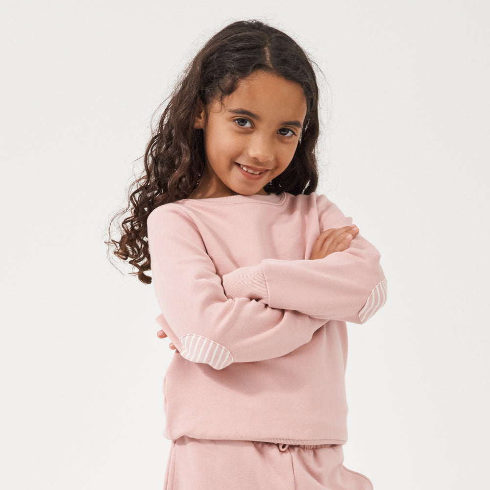 Child folding her arms showing off the elbow patches on her Mauve Blush crewneck