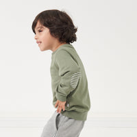 Side view image of a child wearing a Moss elbow patch crewneck detailing the elbow patches