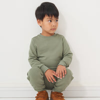 Child leaning against a wall wearing a Moss elbow patch crewneck and matching joggers