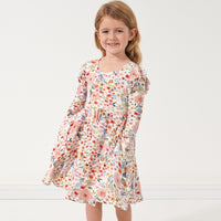 Child posing with her hands in her pockets wearing a Mauve Meadow printed twirl dress