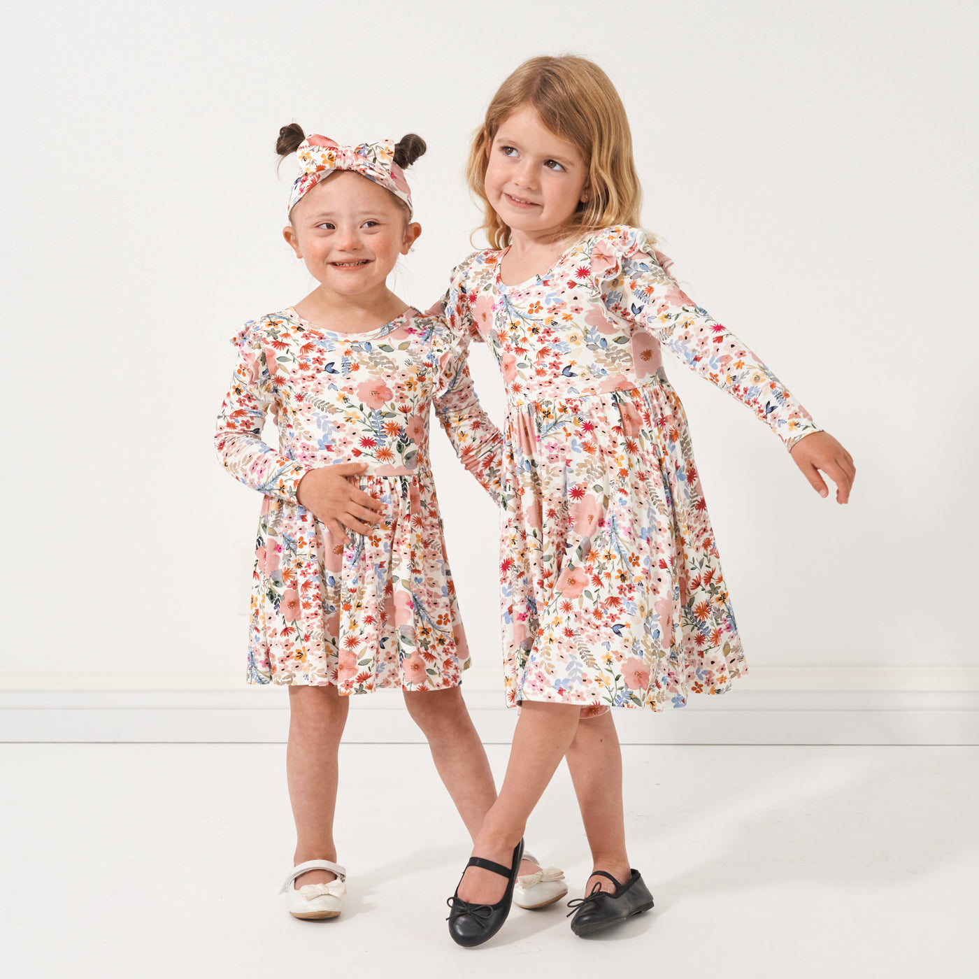 Two children posing together wearing matching Mauve Meadow printed twirl dress and twirl dress with bodysuit paired with a matching luxe bow headband