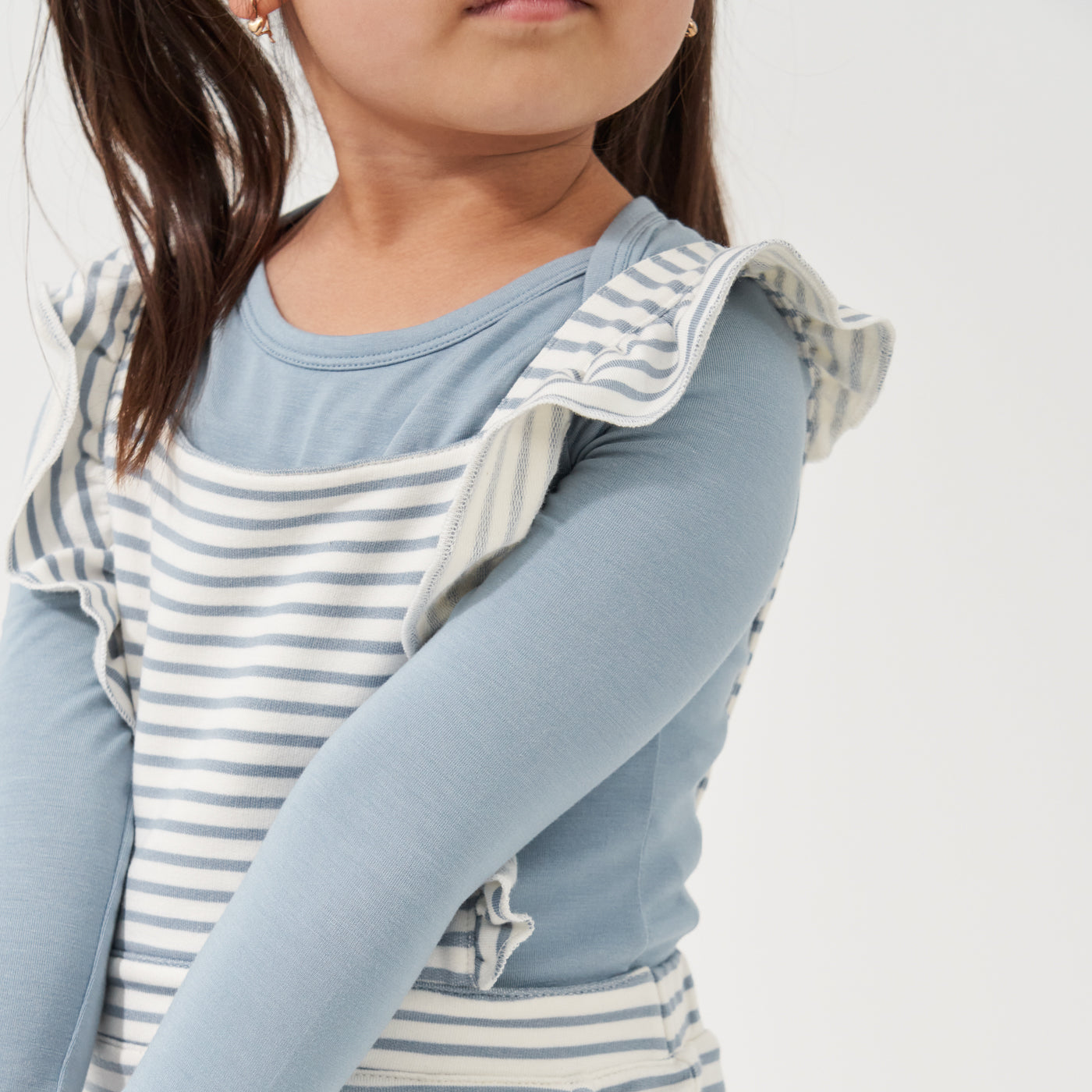 Alternate close up image of a child posing wearing Ivory and Fog Striped ruffle overalls paired with a Fog classic tee detailing the ruffled straps 
