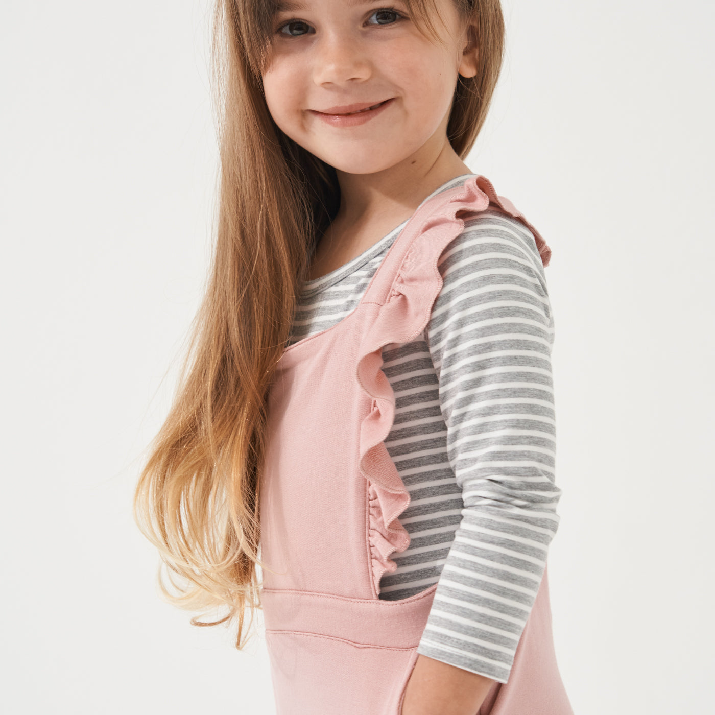 close up profile image of a child wearing Mauve Blush overalls over a Heather Gray Striped classic tee