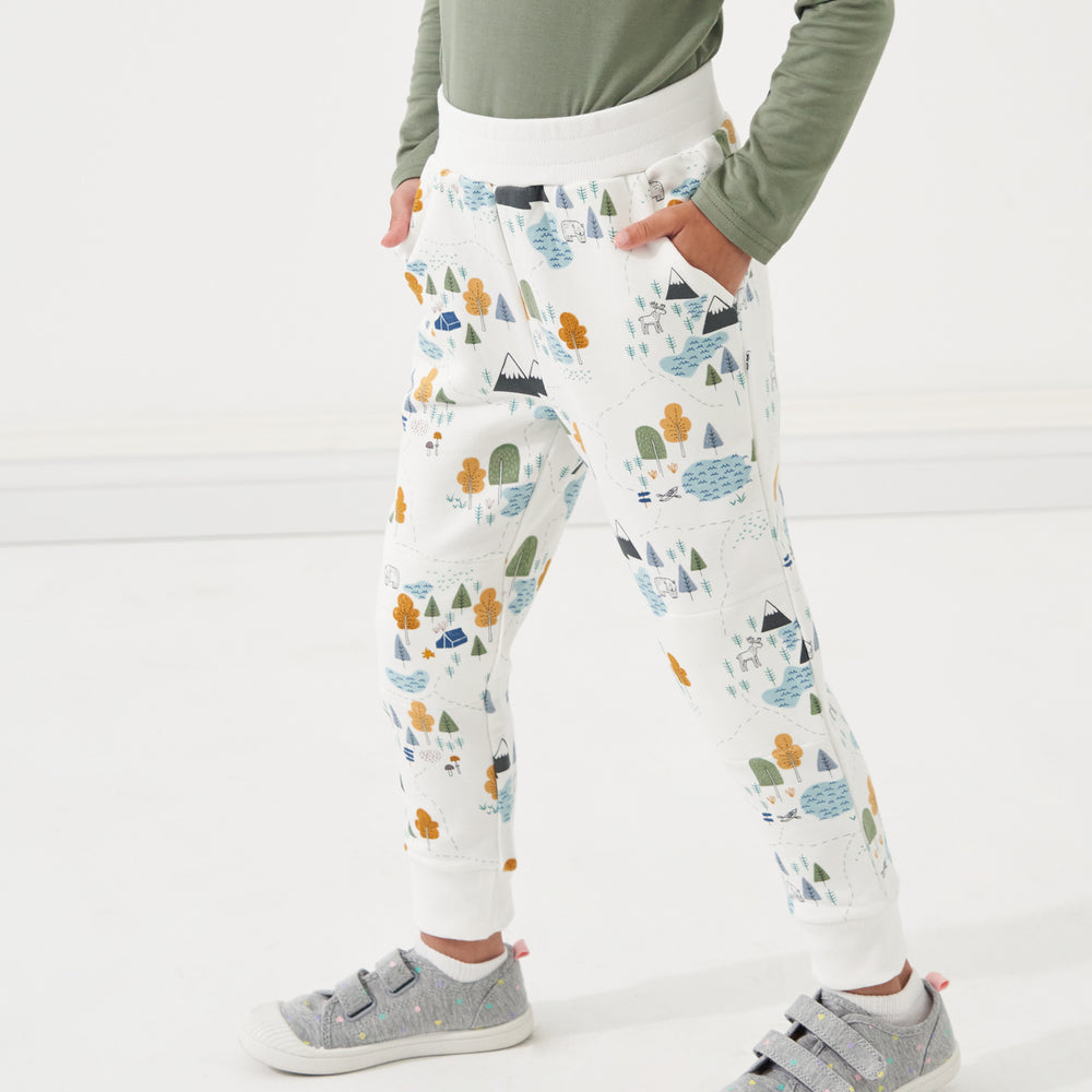 Click to see full screen - Child standing with their hands in their pockets wearing Let's Explore printed joggers