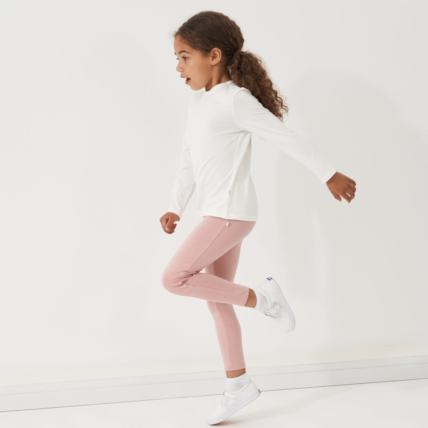 Profile view of a child wearing Mauve Blush leggings paired with an ivory classic tee