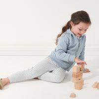 Child playing with blocks wearing a pair of Ivory and Fog Striped leggings paired with a Fog zip hoodie