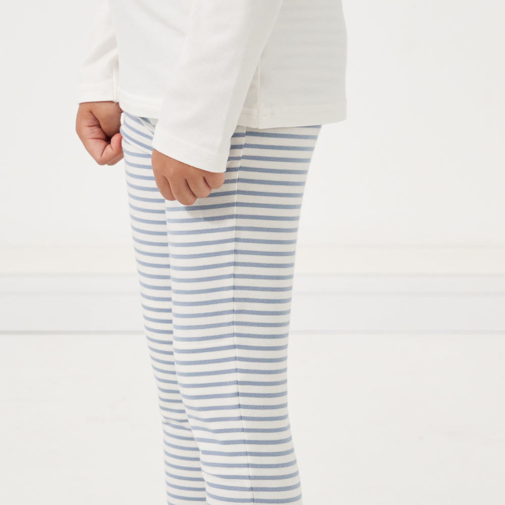 Close up image of a child wearing a pair of Ivory and Fog Striped leggings paired with a Ivory classic tree
