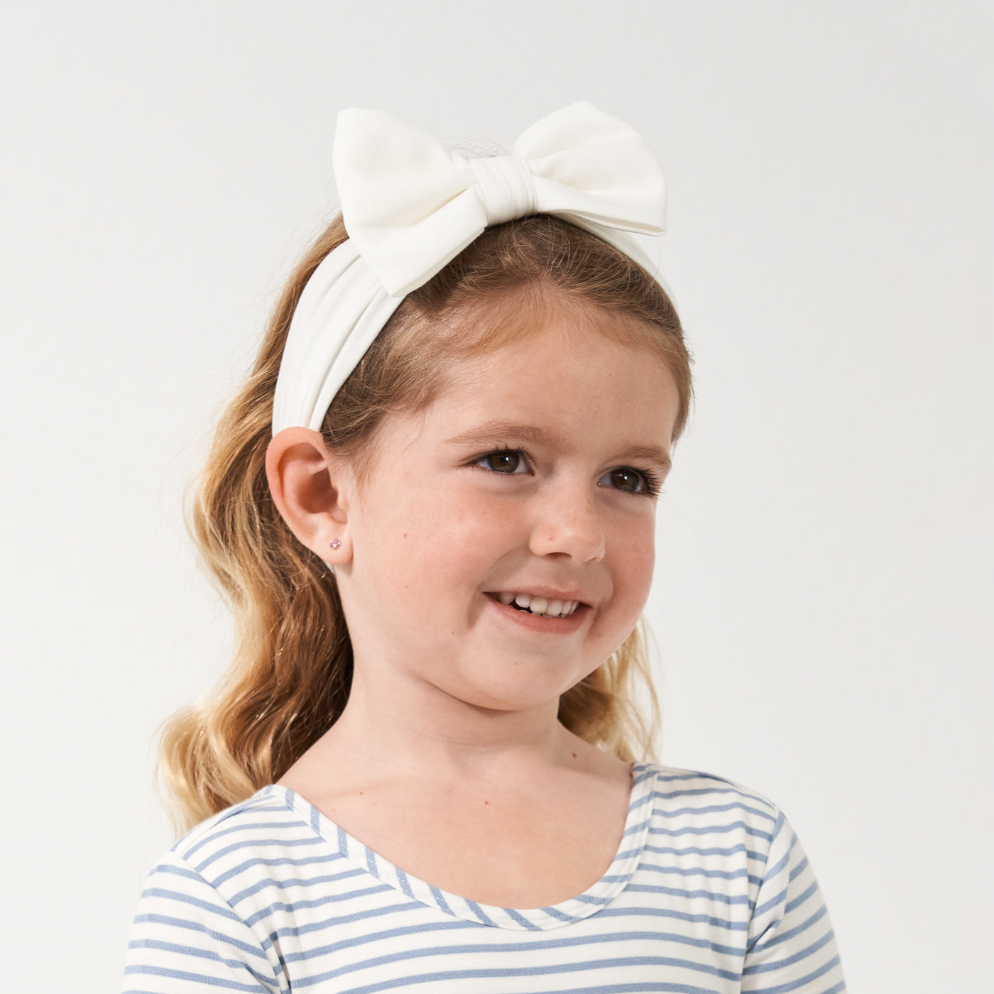 Profile view of a child wearing an Ivory luxe bow headband paired with a Fog and Ivory classic tee