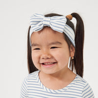 Child wearing an Ivory and Fog Stripe luxe bow headband paired with a matching classic tree