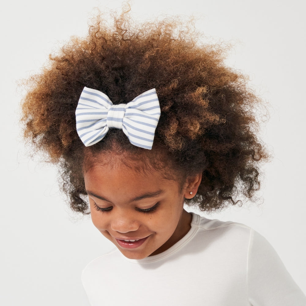 Click to see full screen - Child wearing an Ivory and Fog Stripe luxe bow headband paired with an Ivory classic tree