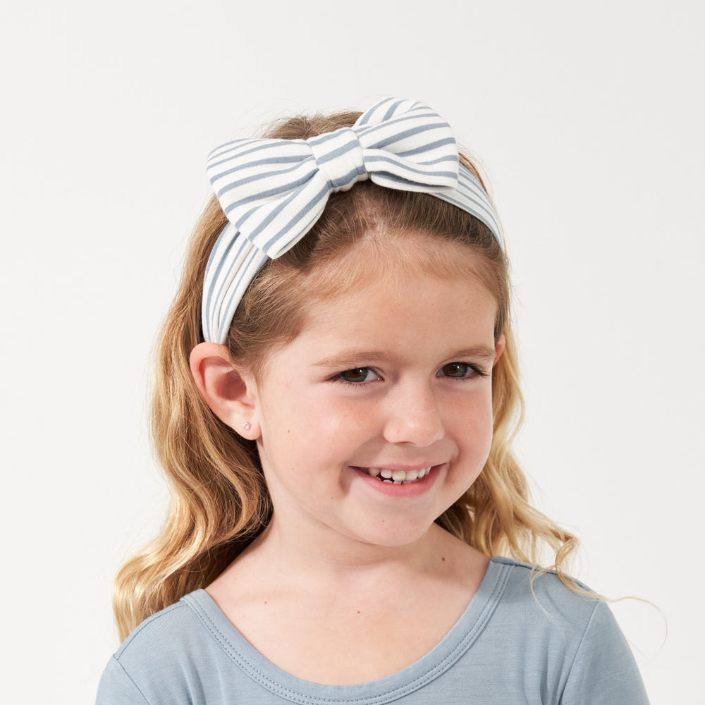 Click to see full screen - Child wearing an Ivory and Fog Stripe luxe bow headband paired with a Fog classic tree