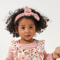Young child wearing a Mauve Blush luxe bow headband paired with Mauve Meadow printed overalls