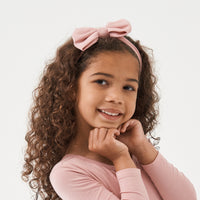 Child posing wearing a Mauve Blush luxe bow headband paired with a Mauve Blush classic tee