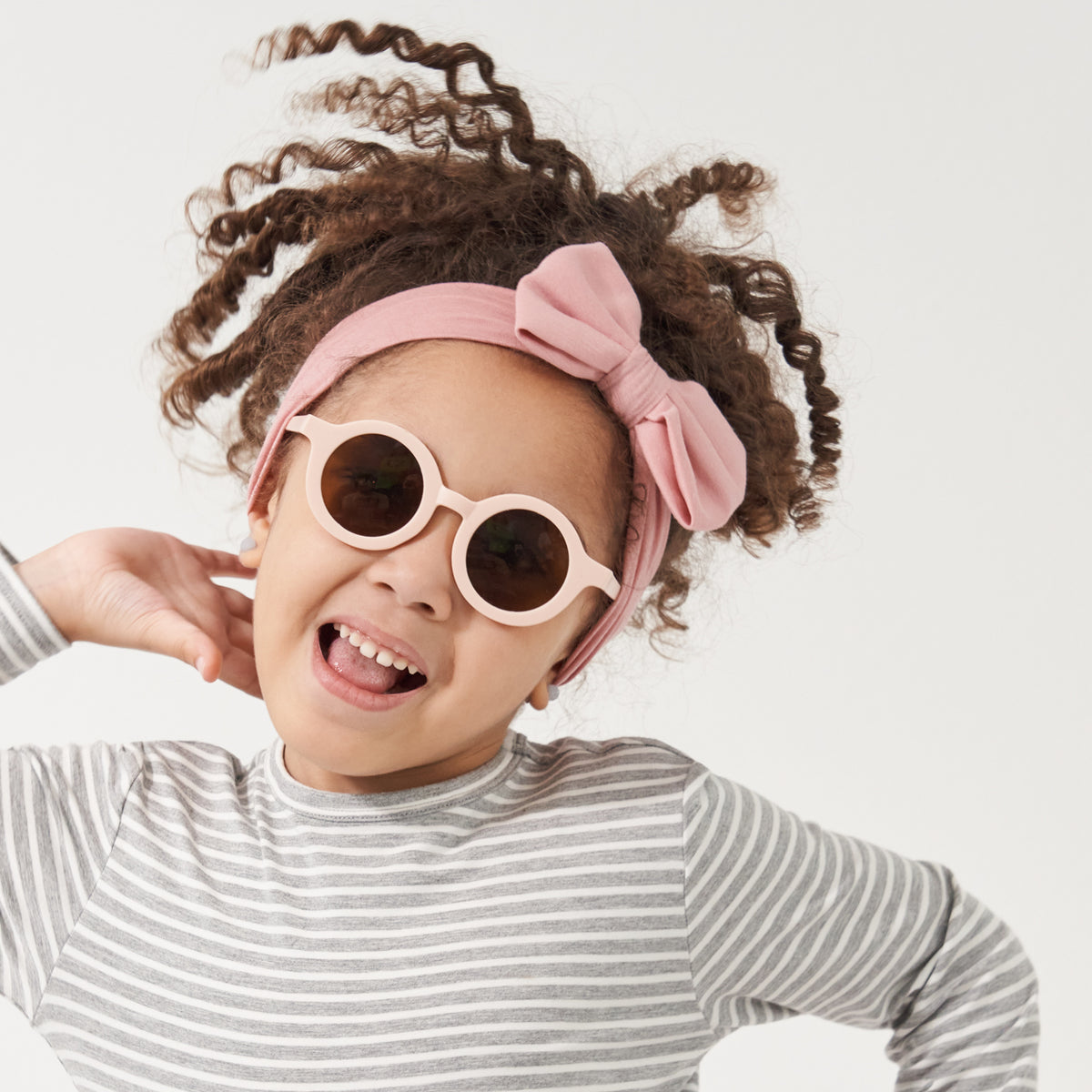 Child posing wearing a Mauve Blush luxe bow headband paired with a Heather Gray Striped classic tee