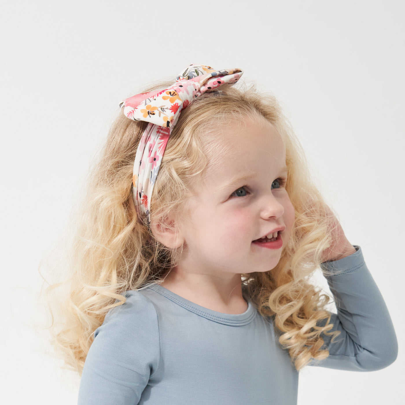Profile view of a child wearing a Mauve Meadow printed luxe bow headband with a Fog play tee