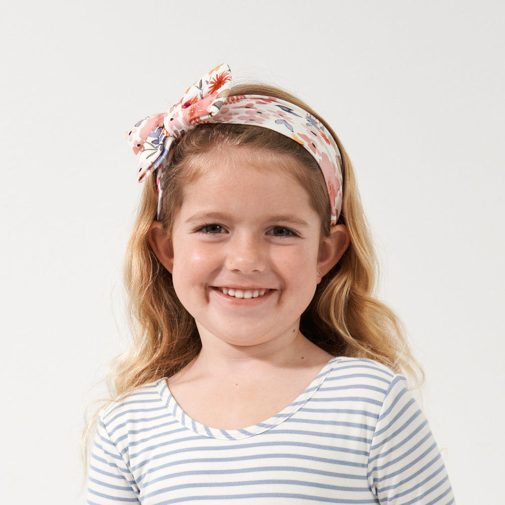 Child wearing a Mauve Meadow printed luxe bow headband paired with a Mauve Meadow and Ivory and Fog Striped twirl dress