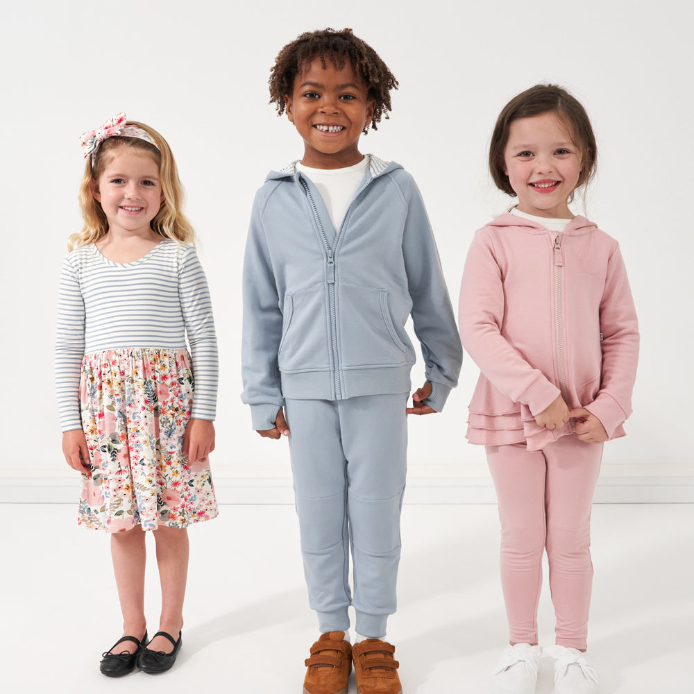 Image of three children wearing a twirl dress, zip hoodies, joggers, and leggings from Play by Little Sleepies