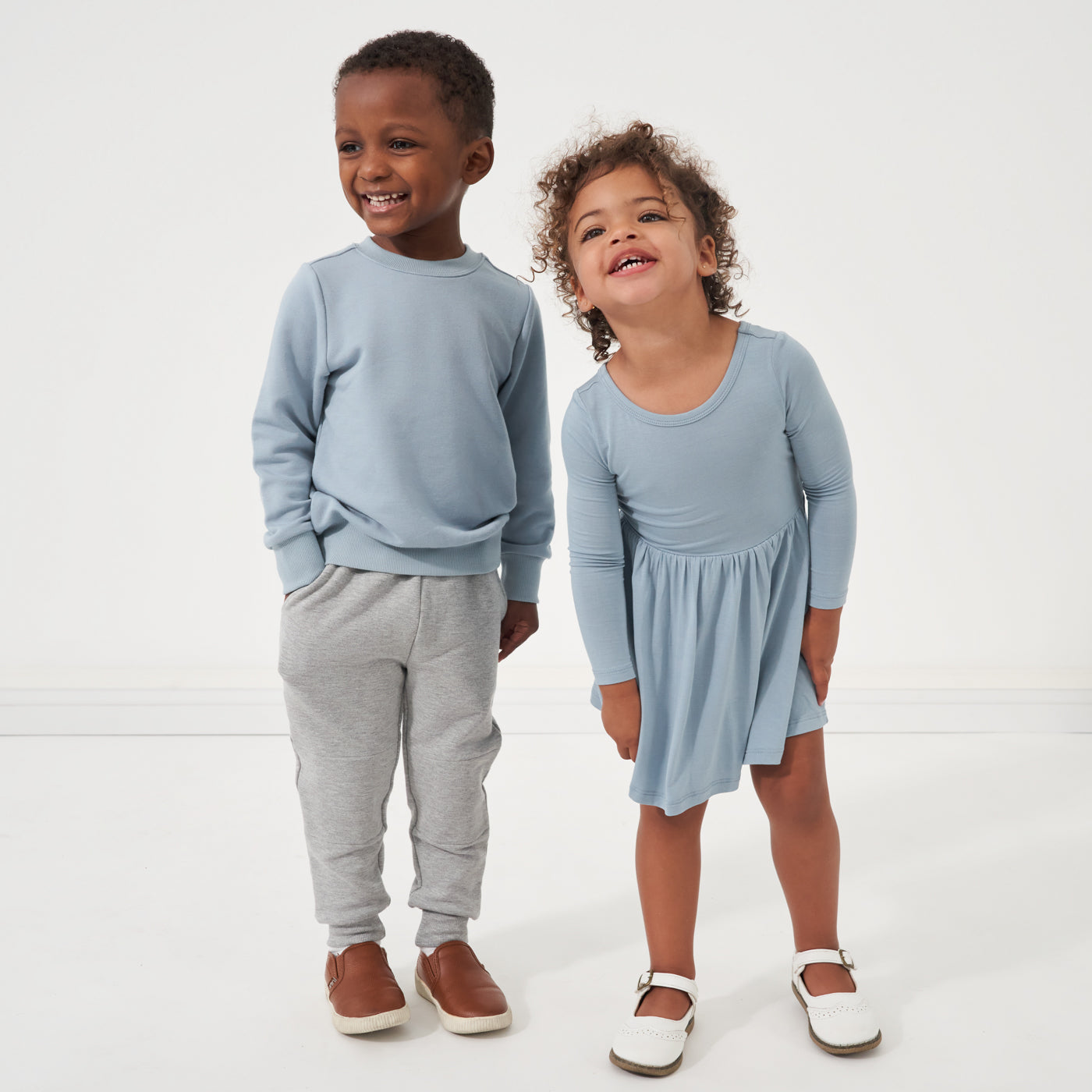 Two children wearing coordinating outfits from Play by Little Sleepies in Fog and Gray