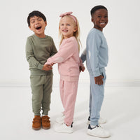 Three children wearing matching elbow patch crewnecks and joggers from Play by Little Sleepies