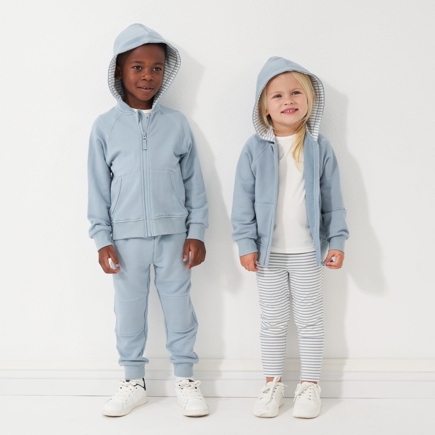 Two children wearing matching Fog zip hoodies and coordinating Fog jogger and Fog Stripe leggings from Play by Little Sleepies