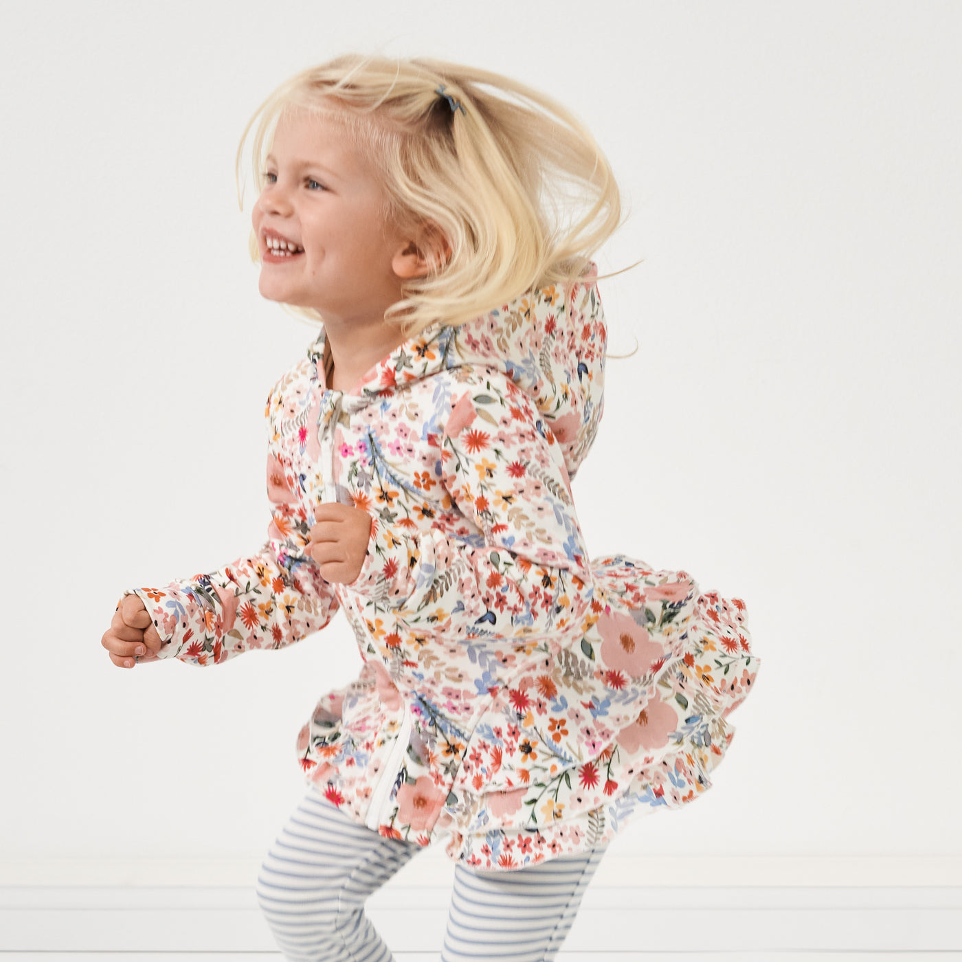 Child jumping showing off her Mauve Meadow printed peplum hoodie paired with Ivory and Fog striped leggings