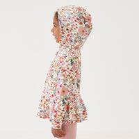 Profile view of a child wearing a Mauve Meadow printed peplum hoodie showing off the hood feature