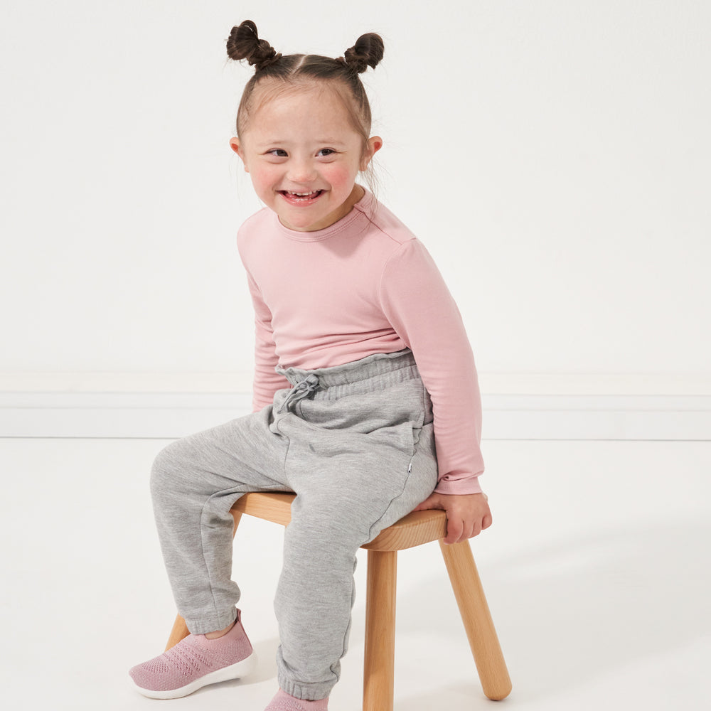 Click to see full screen - Child sitting on a stool wearing Heather Gray paperbag joggers paired with a Mauve Blush classic tee