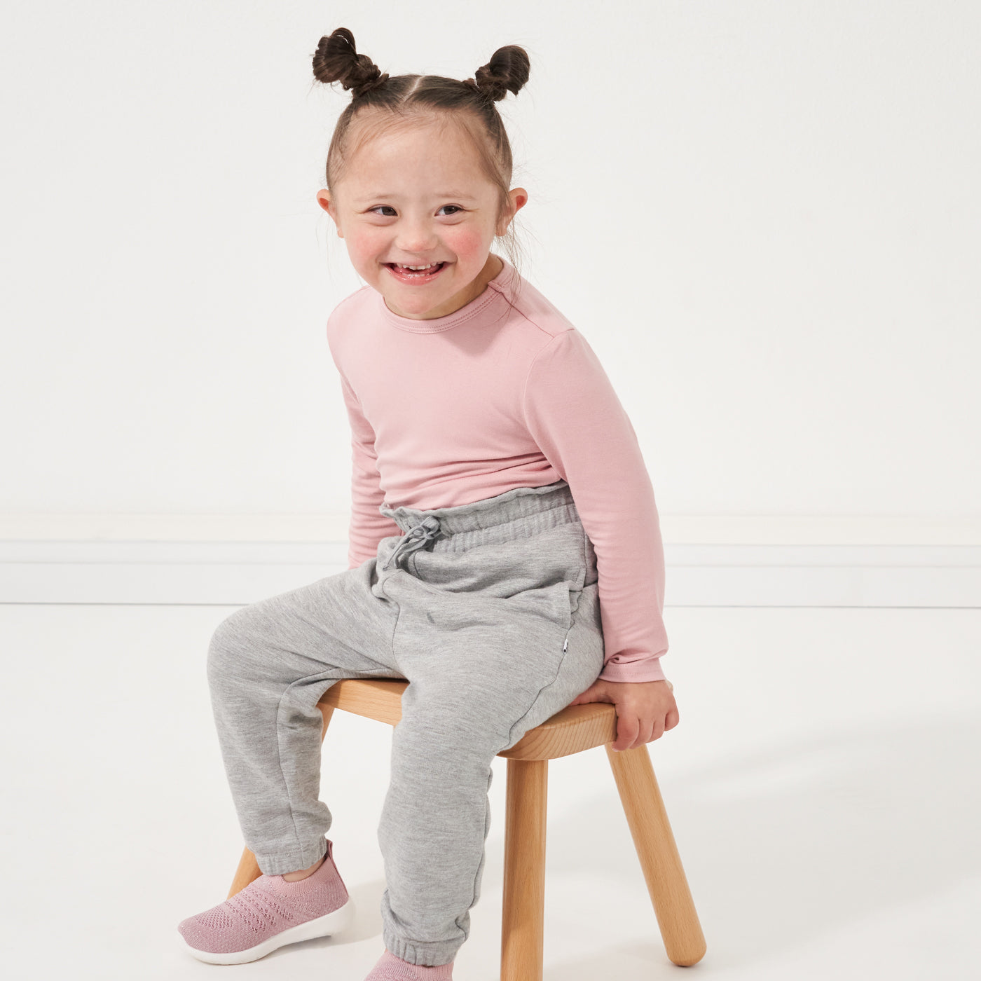 Child sitting on a stool wearing Heather Gray paperbag joggers paired with a Mauve Blush classic tee