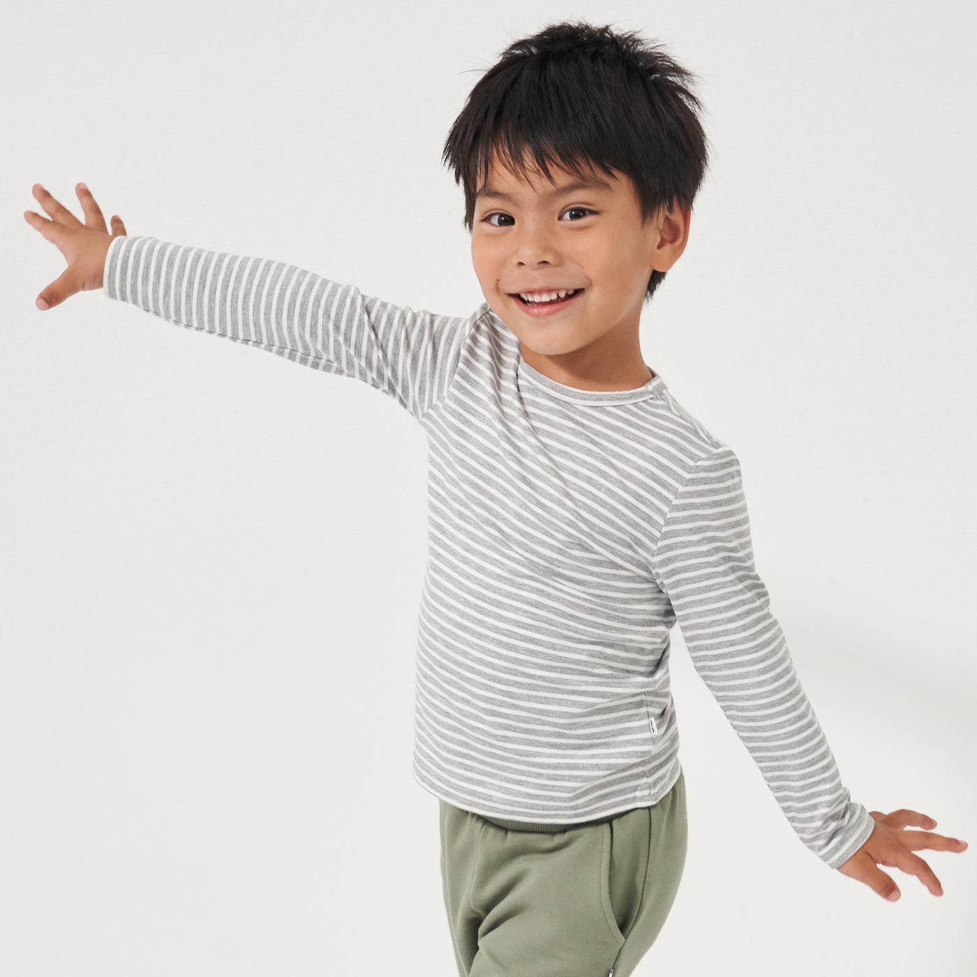 Child posing wearing a Heather Gray and Ivory Stripe classic tee paired with Moss joggers
