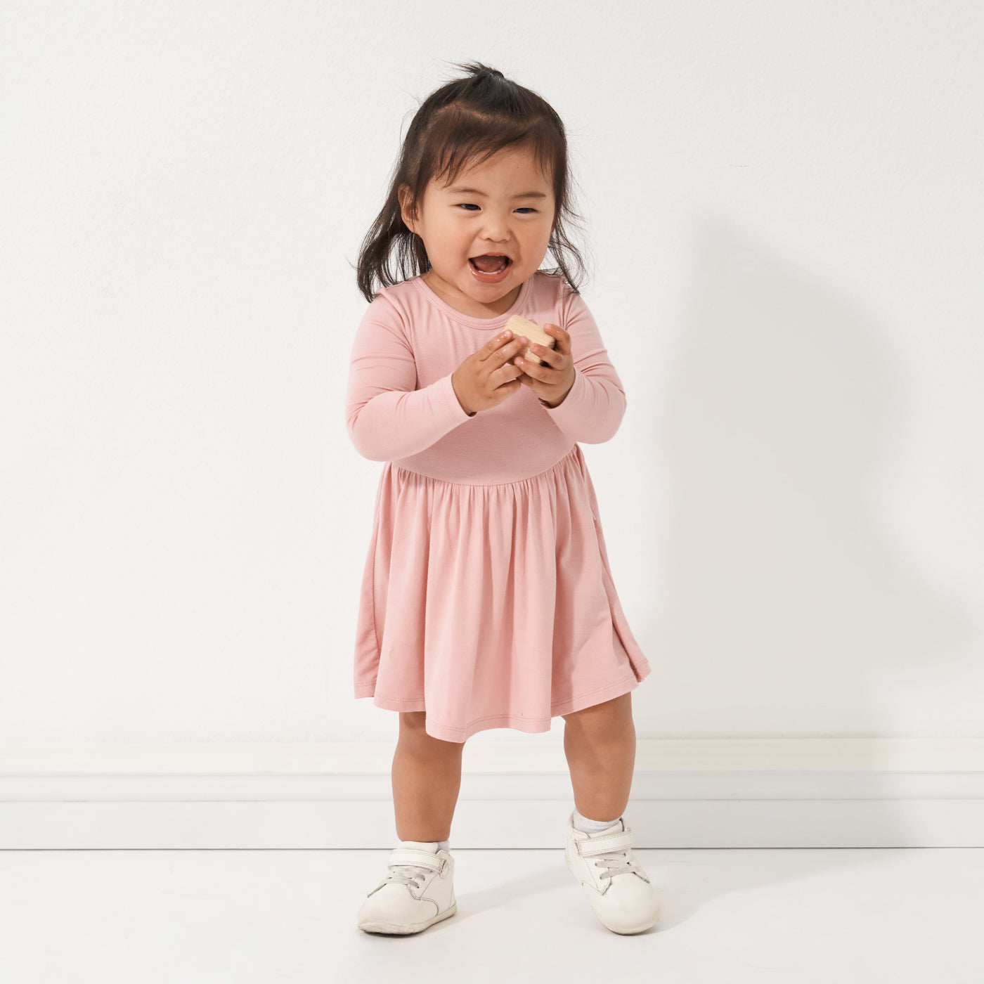 Child playing with a wooden block wearing a Mauve Blush twirl dress with bodysuit