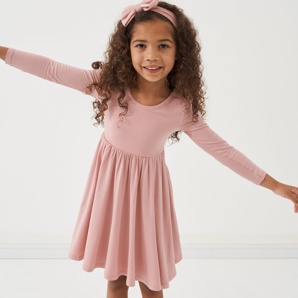 Child posing wearing a Mauve Blush twirl dress paired with a matching luxe bow headband