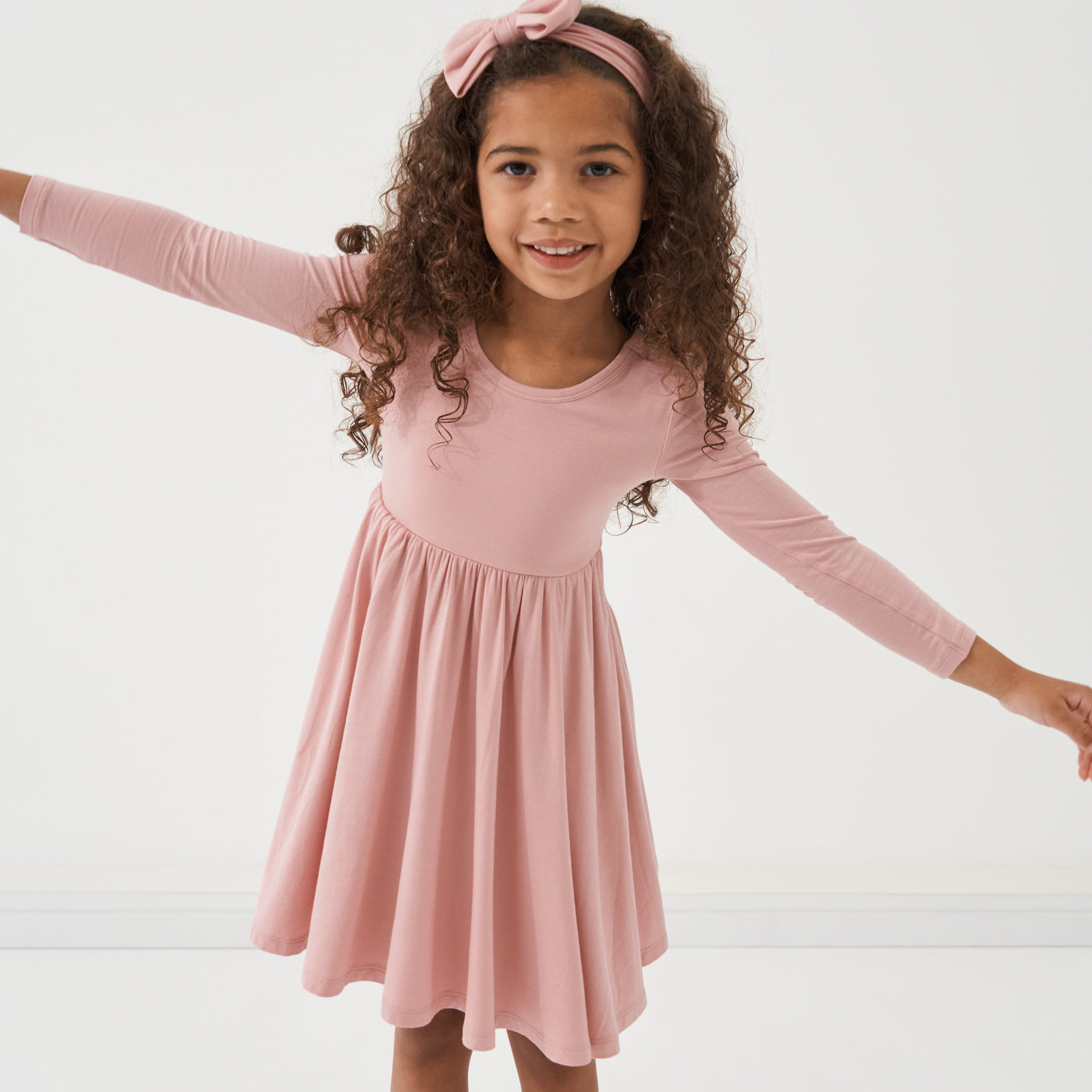 Child posing wearing a Mauve Blush twirl dress paired with a matching luxe bow headband