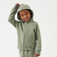 Child wearing a Moss zip hoodie with the hood over their head
