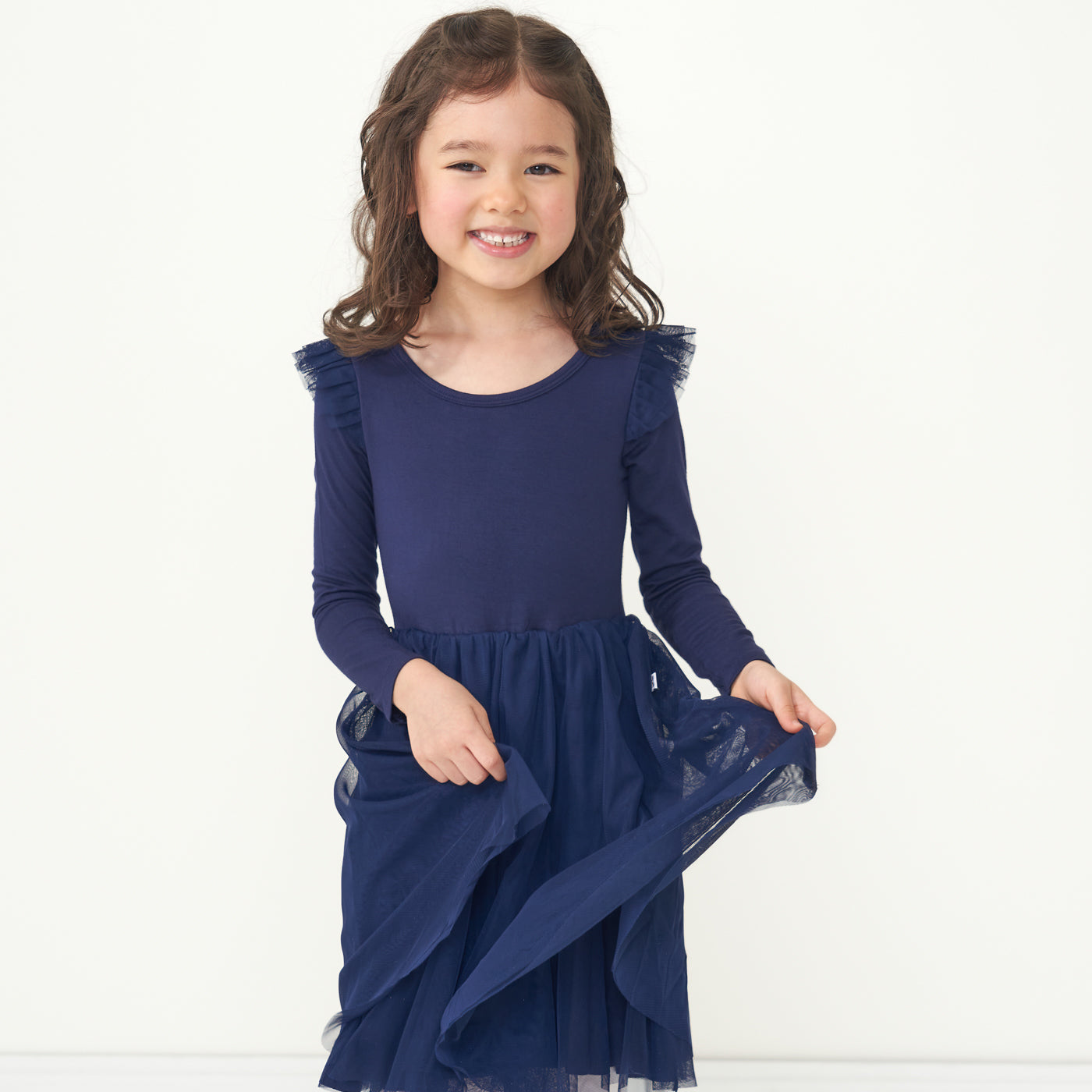 Child holding up the outer layer of the Classic Navy flutter tutu dress she is wearing
