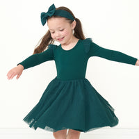 Child twirling wearing an Emerald flutter tutu dress paired with an Emerald luxe bow headband