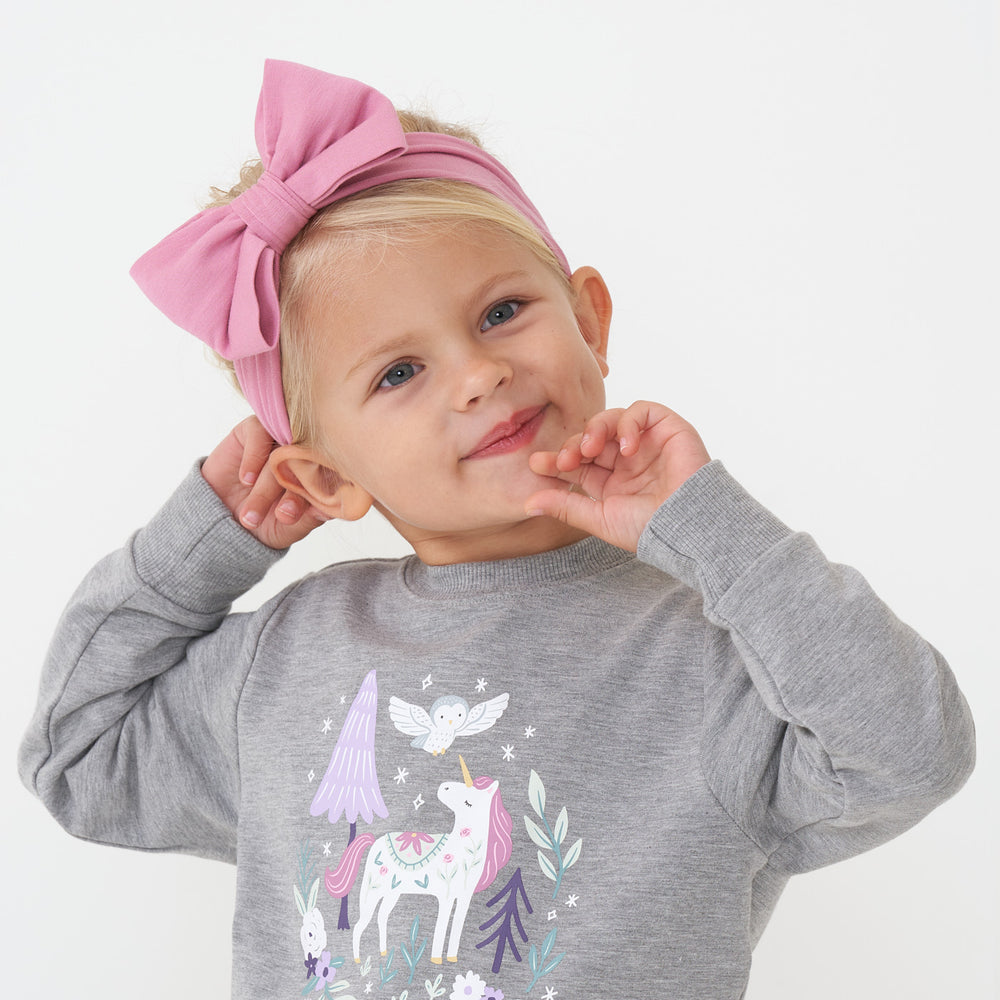 Close up image of a child wearing a Garden Rose luxe bow headband paired with a Unicorn crewneck sweatshirt