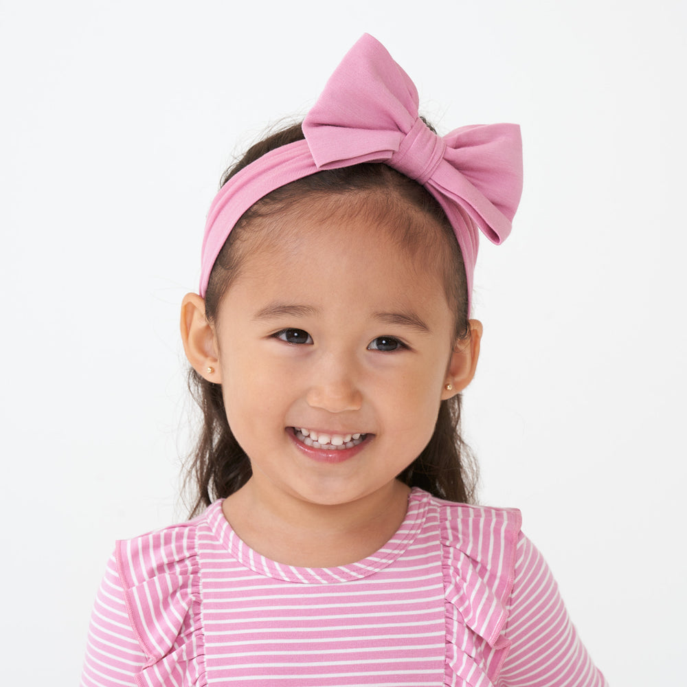 Close up image of a child wearing a Garden Rose luxe bow headband paired with a Garden Rose Stripe flutter tee