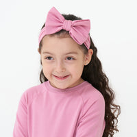 Close up image of a child wearing a Garden Rose luxe bow headband paired with a Garden Rose drop waist dress