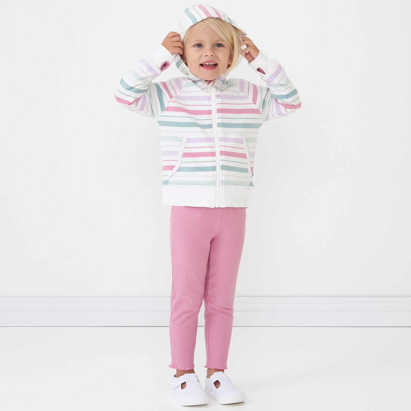 Child playing wearing a Garden Rose ribbed lettuce legging paired with a winter stripes zip hoodie