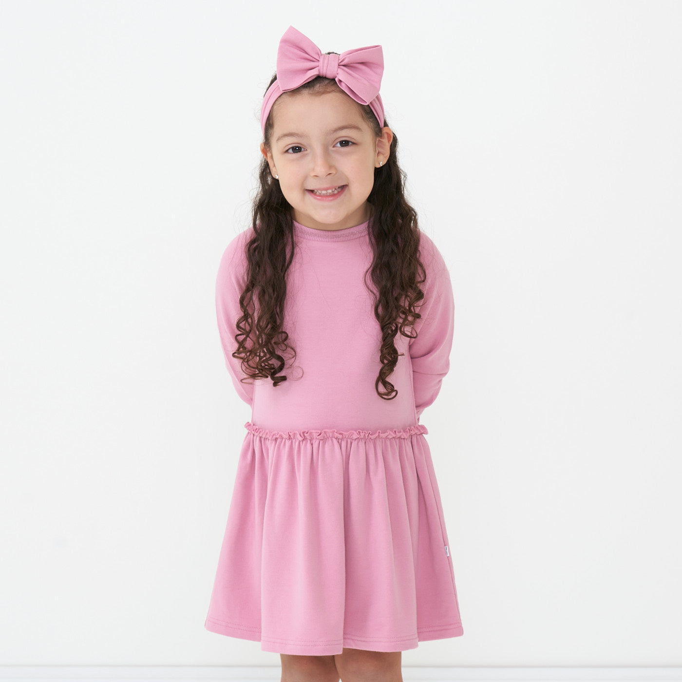 Child posing wearing a Garden Rose drop waist dress paired with a Garden Rose luxe bow headband