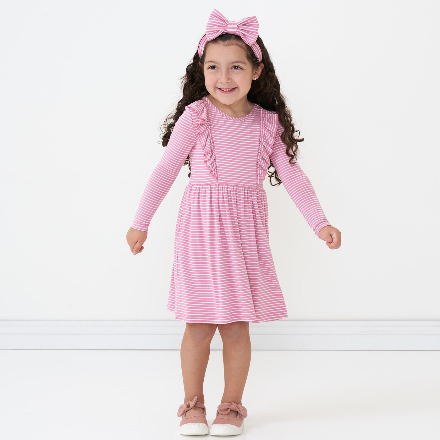 Child wearing a Garden Rose Stripes ruffle bib skater dress wearing a matching luxe bow headband
