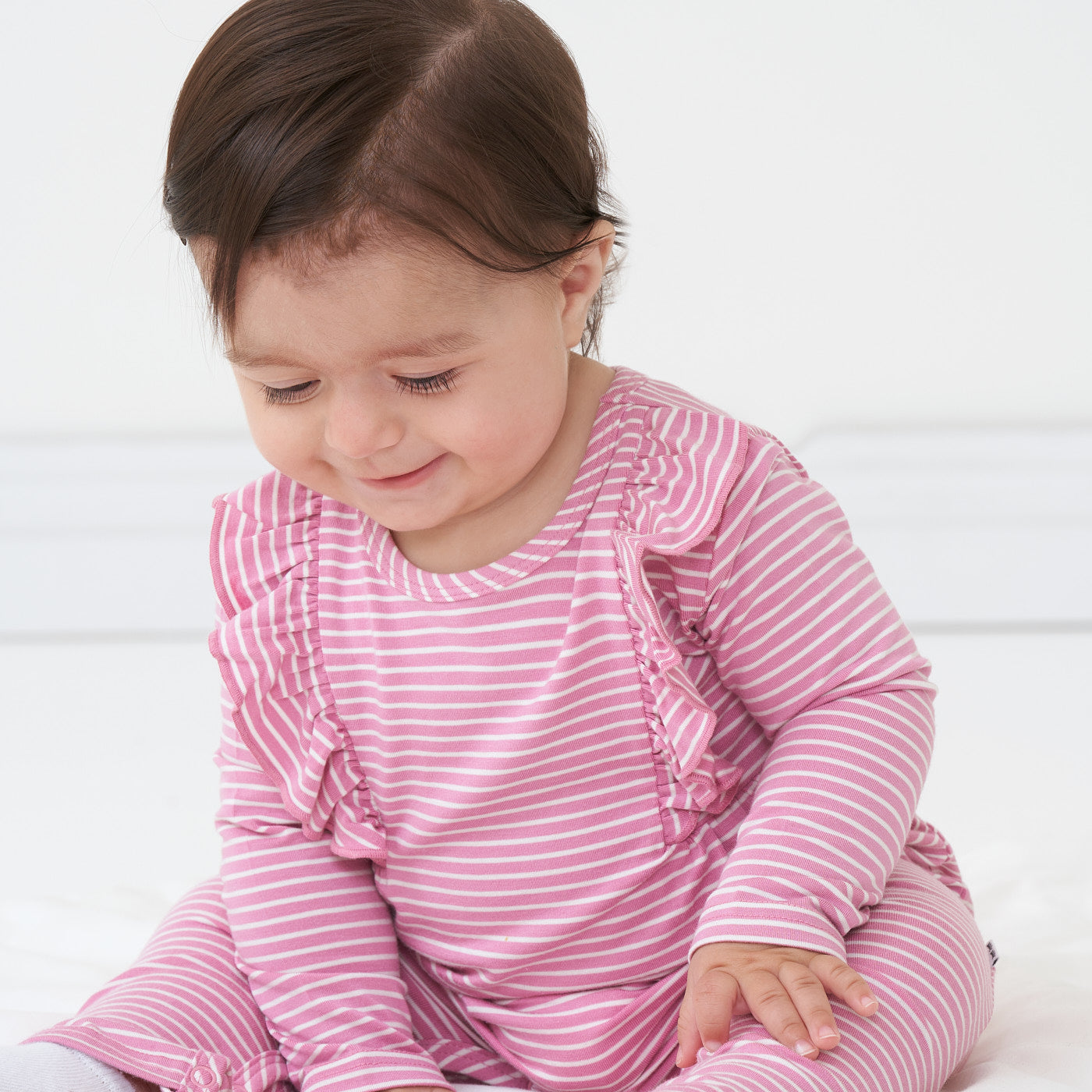 Close up image of a child sitting wearing a Garden Rose stripe ruffle bib romper