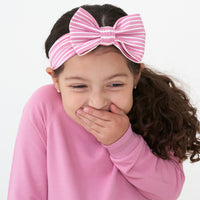 Close up image of a child wearing a Garden Rose Stripe luxe bow headband paired with a Garden Rose drop waist dress 