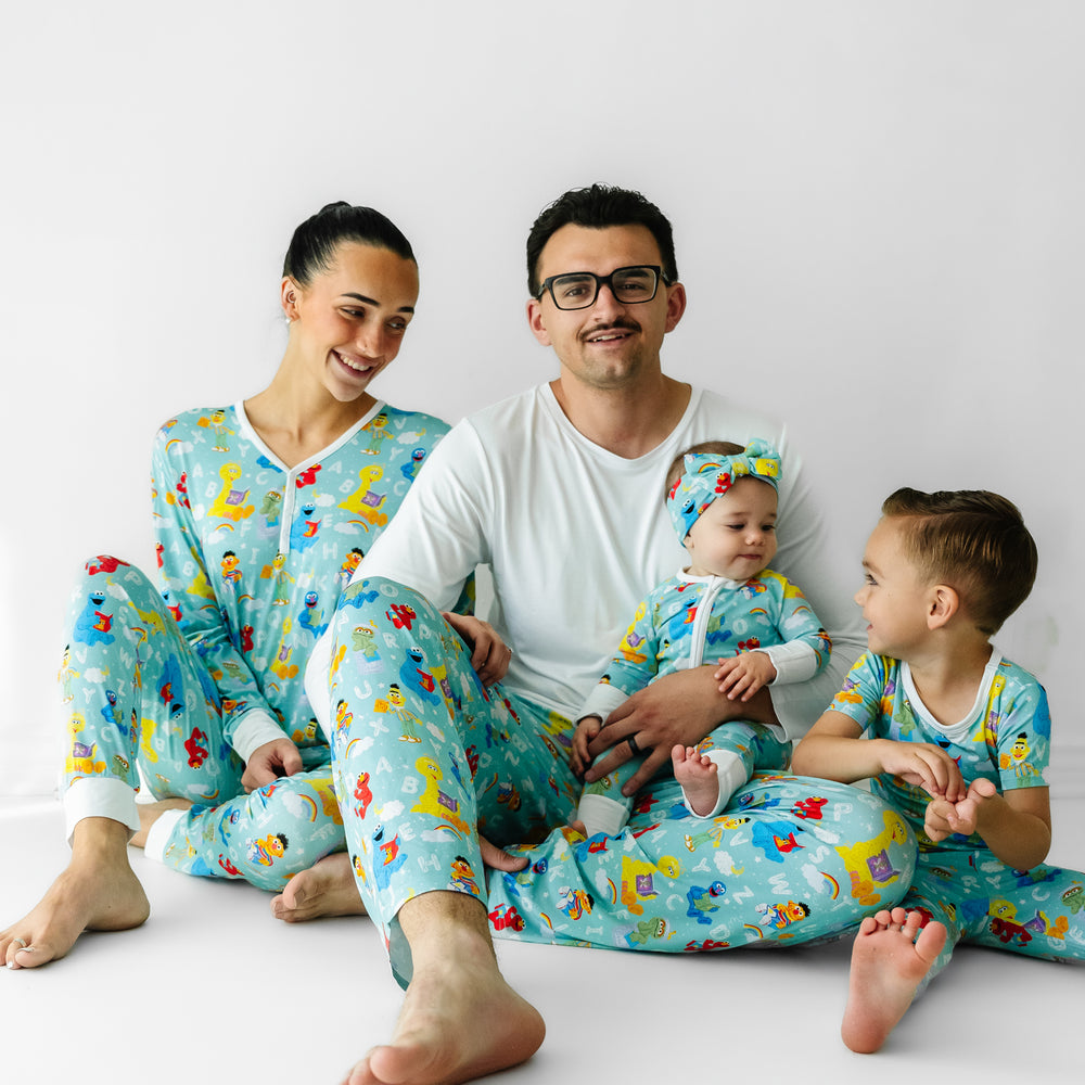 Family of four sitting on the ground wearing matching Spelling with Sesame Street pajamas