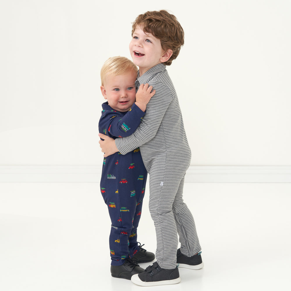 Two children hugging. One is wearing a Tree Traffic polo romper and the other child is wearing a Heather Charcoal Stripes polo romper