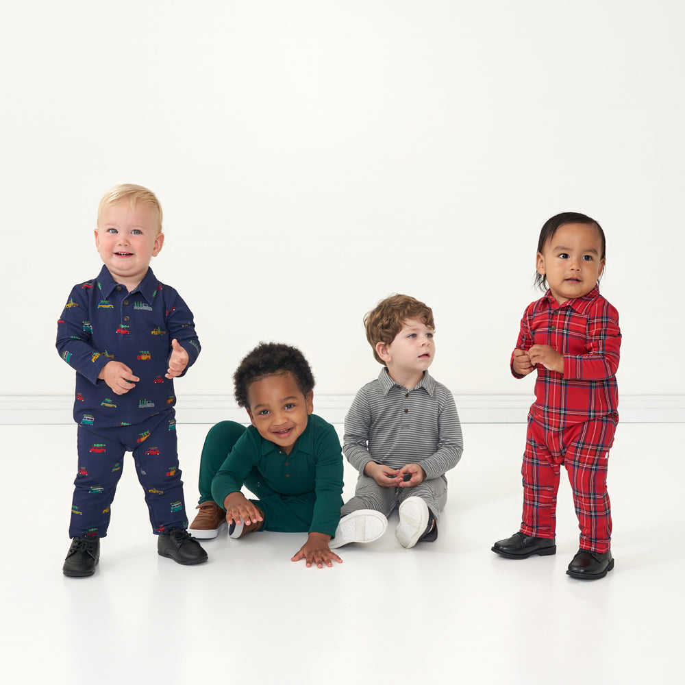 Four children sitting together wearing coordinating Holiday play polo rompers in the following prints: Tree Traffic, Emerald, Heather Charcoal Stripes, Holiday Plaid