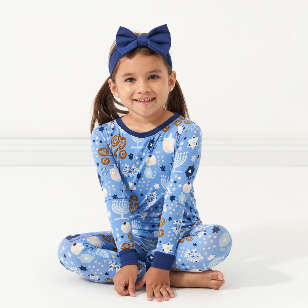 Child sitting wearing Hanukkah Lights and Love two piece pajama set paired with a Sapphire luxe bow headband