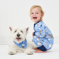 Small white dog wearing a Hanukkah Lights and Love pet bandana. Next to him is a small child wearing a matching Hanukkah Lights and Love zippy
