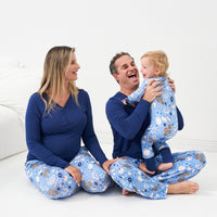 Family of three posing together wearing Hanukkah Lights and Love pajama sets. Dad is wearing Hanukkah Lights and Love men's pajama bottoms and Sapphire men's long sleeve pajama top. Mom is wearing Hanukkah Lights and Love women's pajama bottoms and women's Sapphire long sleeve pajama top. Child is wearing a Hanukkah Lights and Love zippy