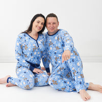Man and woman sitting together wearing Hanukkah Lights and Love pajamas. Woman is wearing Hanukkah Lights and Love women's pajama top paired with matching women's pajama bottoms. Man is wearing Hanukkah Lights and Love men's Lights and Love men's pajama top paired with matching men's pajama bottoms